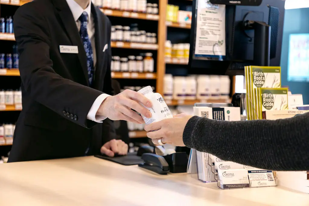 Close-up of wellness specialist handing a supplement bottle to a customer.