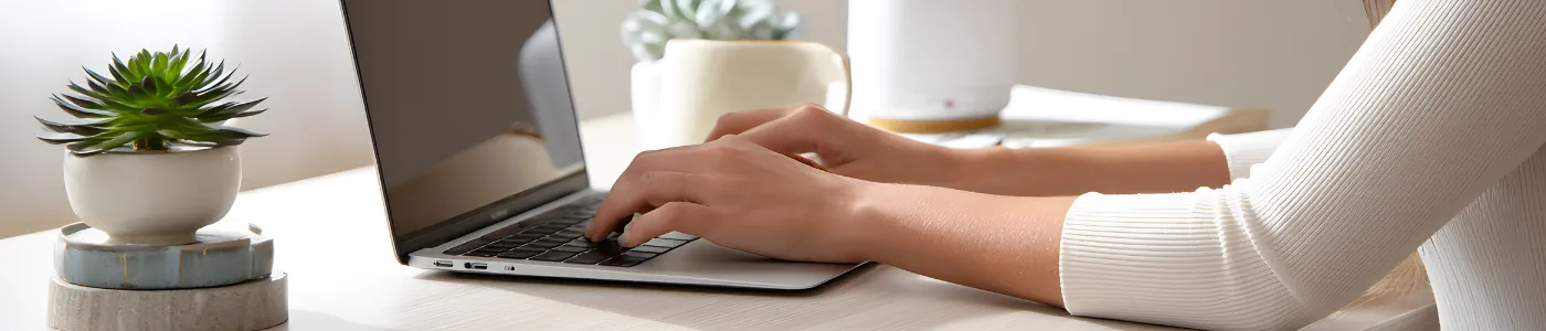 Woman typing on laptop with a plants in the background.