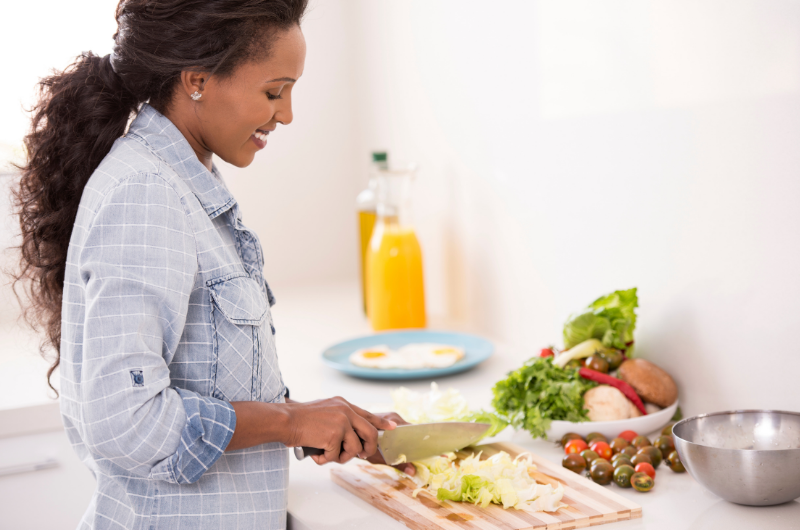 Woman cutting lettuce with more vegetables in the background.